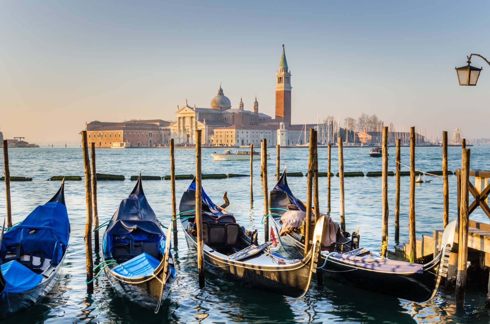 Photo of  Venice at Sunset. Some traditional gondolas, tied up to the quay in Saint Mark's square, are in foreground while Saint George Island, one of the island of Venice, is visible in  background.